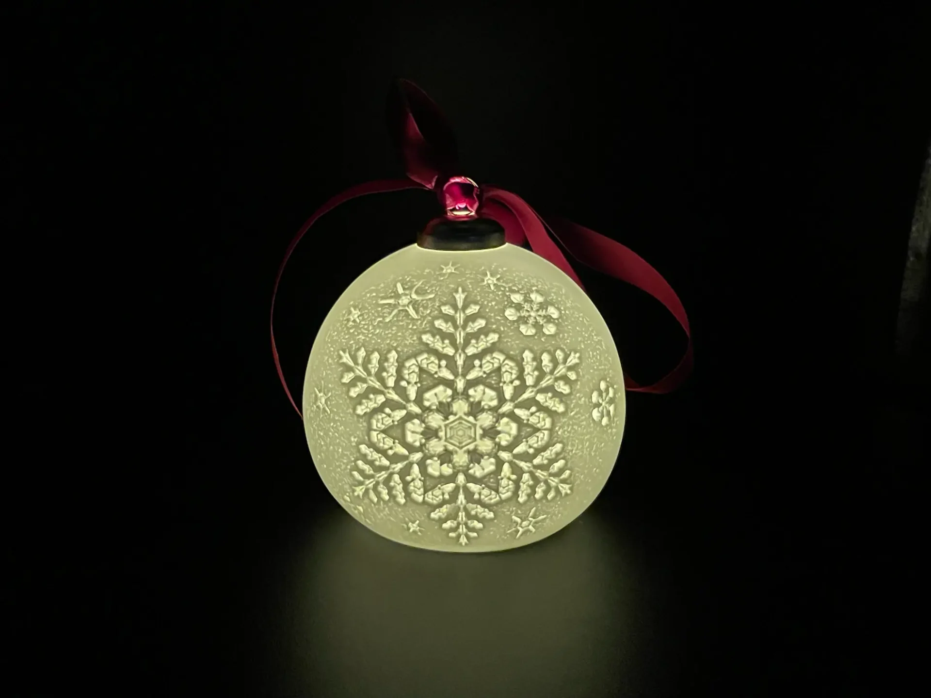 A white christmas ornament with red ribbon on it.